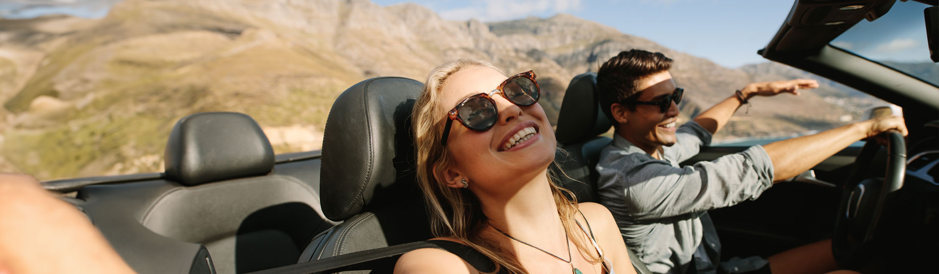 Ein Paar fährt fröhlich in einem Cabrio und genießt die Sonne und die frische Luft.